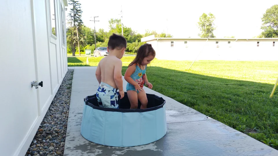 Two young children splash in a wading pool on the walkway outside the units