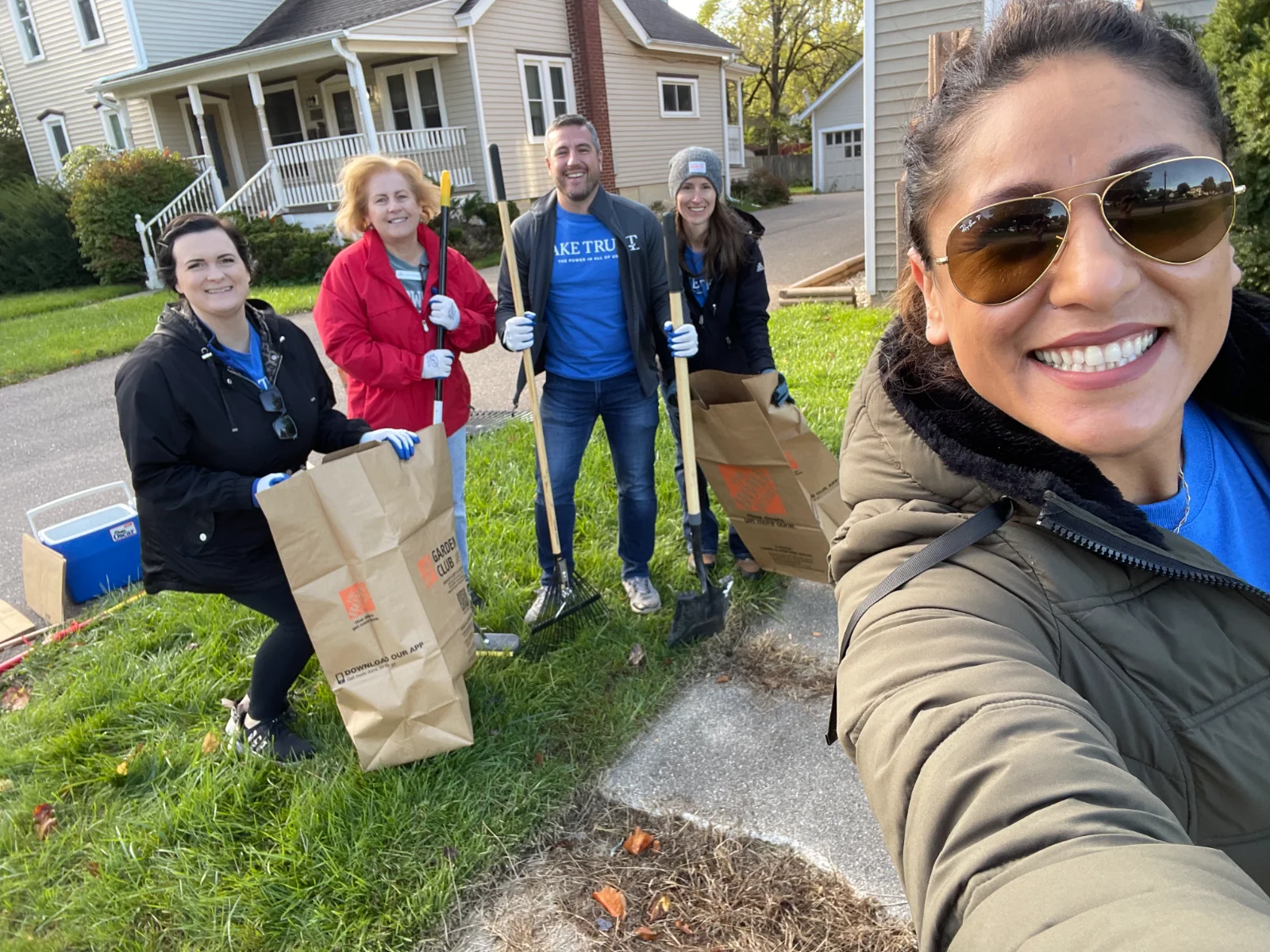 Volunteers with rakes and yard-waste bags outside a home